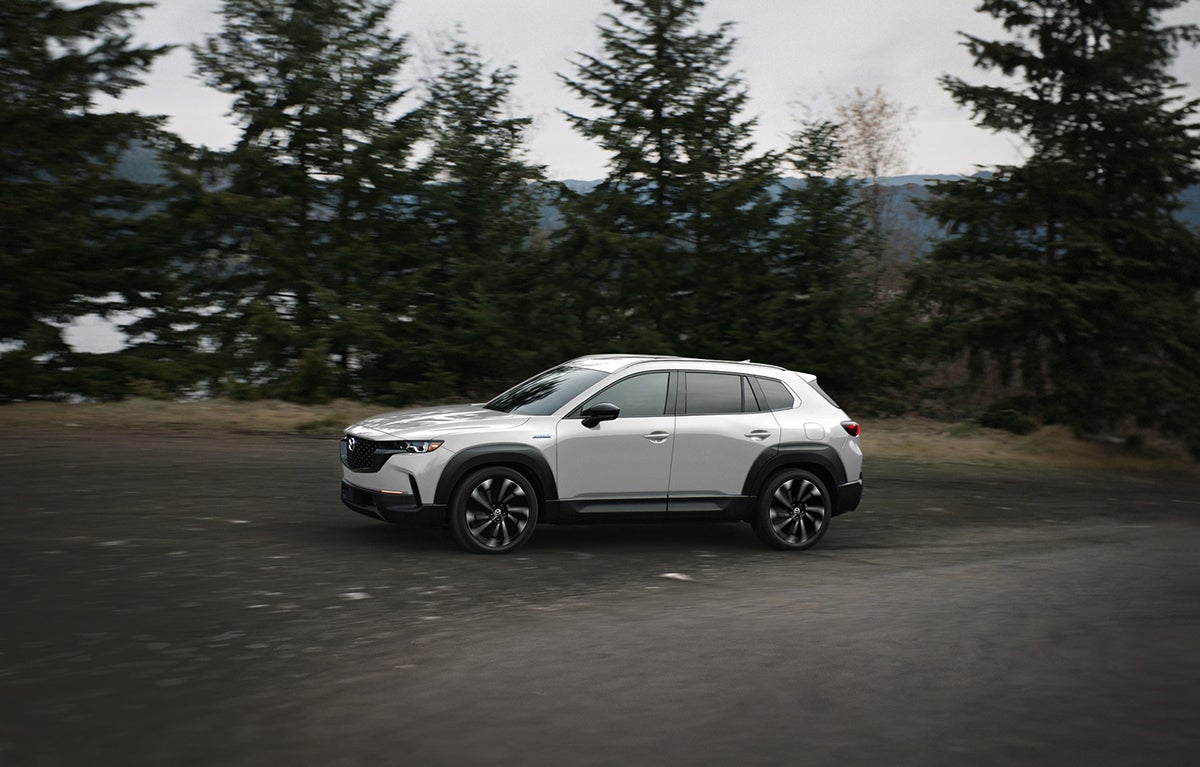 Mazda driving in forest with trees in background